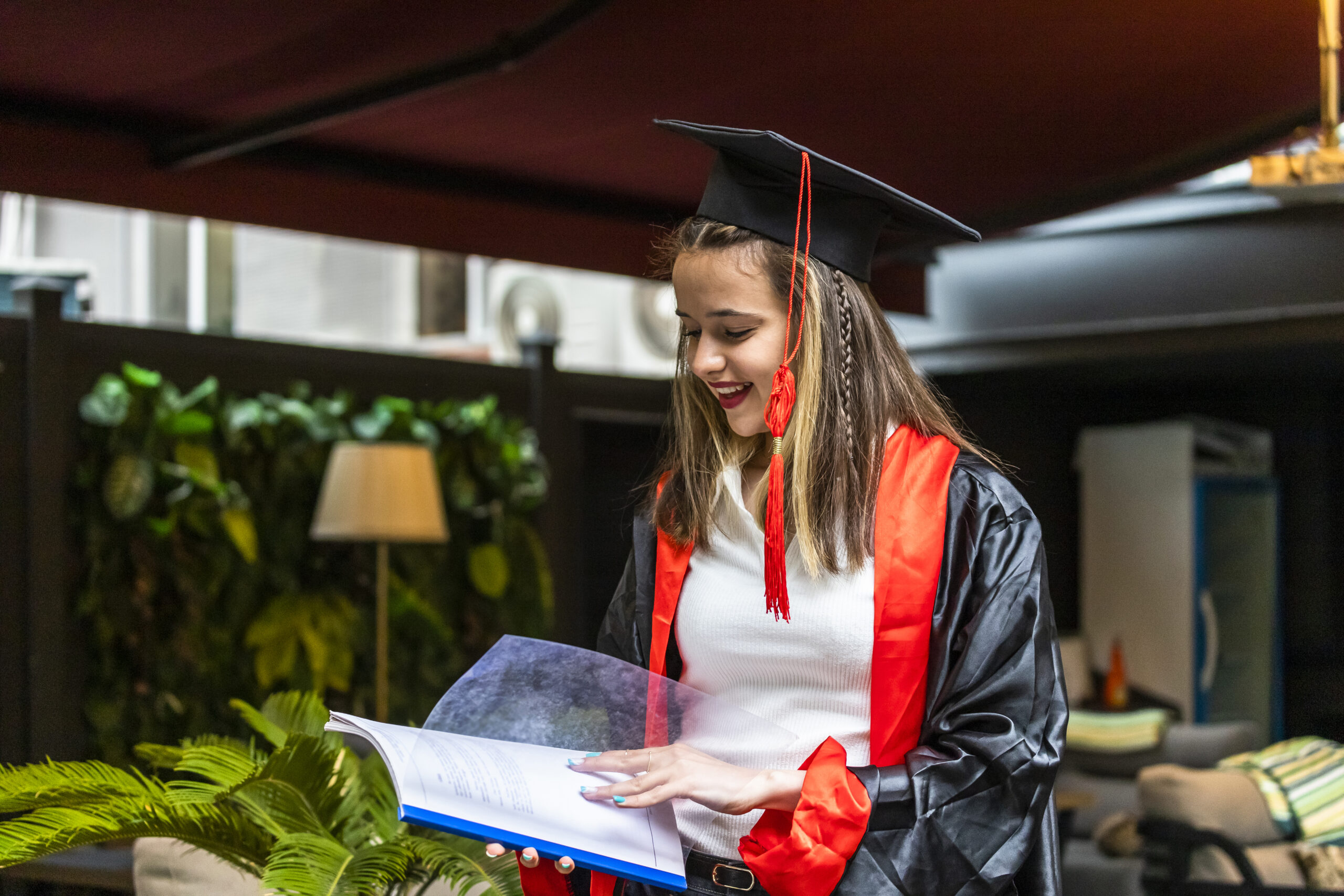 young student wearing graduation cape looking her notebook scaled