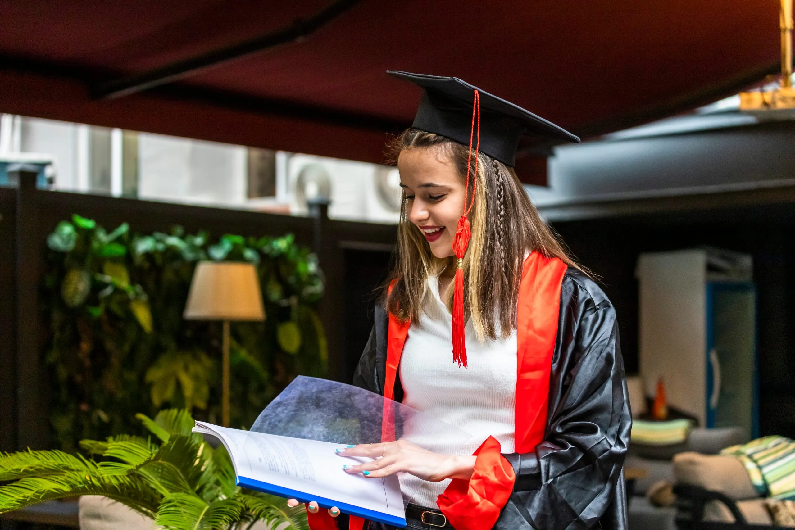 young student wearing graduation cape looking her notebook scaled result
